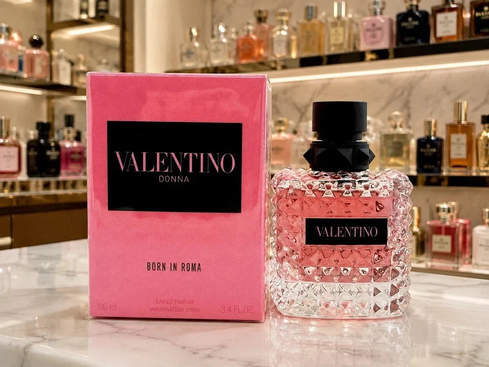 Valentino Donna Born in Roma perfume bottle and its pink box displayed on a marble counter with a blurred background of perfume bottles.